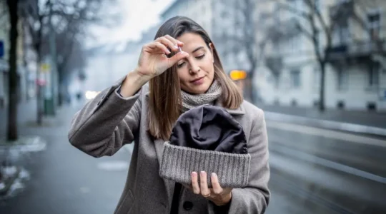 Une femme applique un soin protecteur sur ses longueurs avant de mettre son bonnet doublé sur un trottoir suisse en hiver.